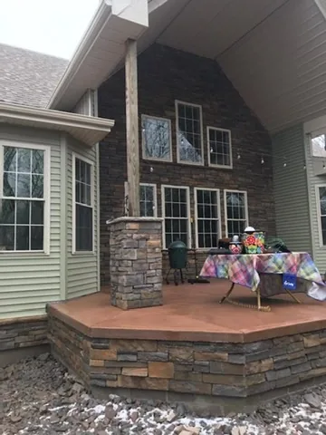 Raised concrete deck with a stacked stone face and a stone column beside a house