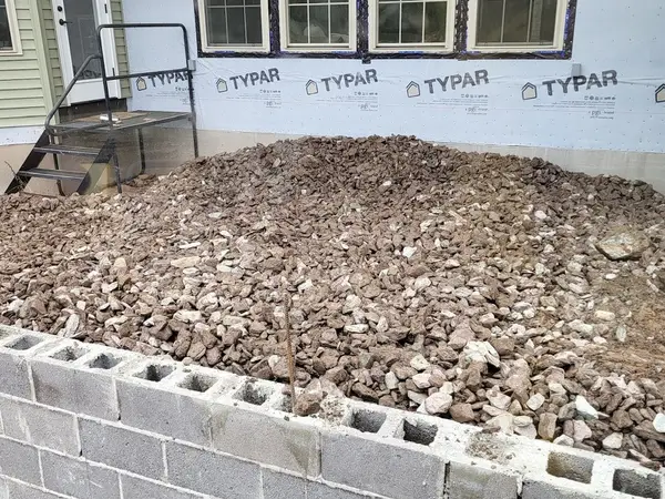 Concrete block foundation wall backfilled with stone beside a new home