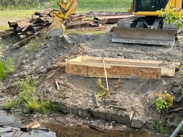 Excavator working beside the stream with old bridge timbers piled behind
