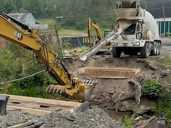 Concrete truck pouring at the bridge site with an excavator alongside