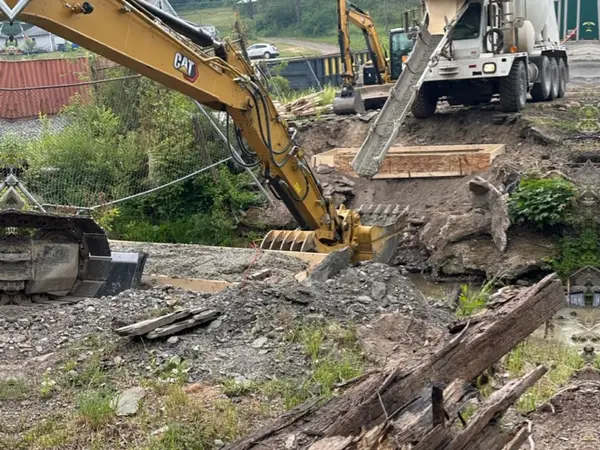 Excavator and concrete truck working beside the removed bridge timbers