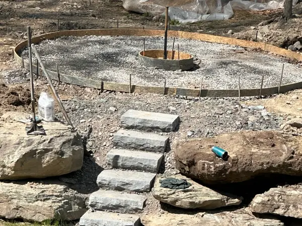 Round fire pit pad being formed above a boulder wall and stone steps