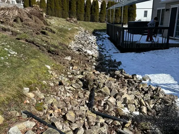 Sloped backyard with loose rock and old drainage pipe before excavation
