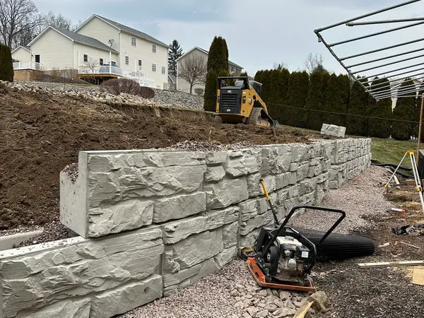 Lower Magnum Stone wall rising, with a plate compactor on the gravel base