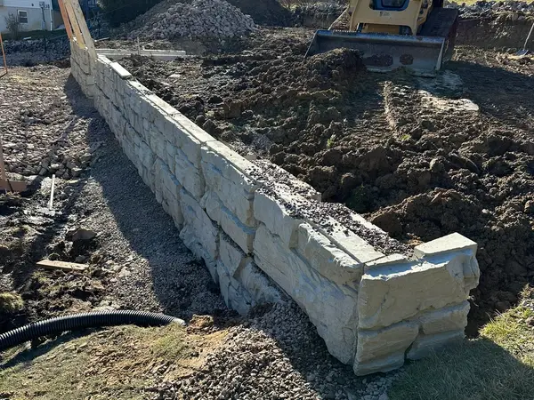Skid steer backfilling behind a long run of Magnum Stone blocks